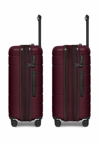 Valigia rigida da cabina di colore bordeaux con superficie texture, zip nere, maniglia laterale e quattro ruote per una facile manovrabilità.