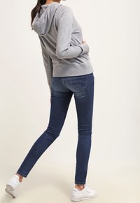 Sudadera gris con capucha, combinada con jeans ajustados de color azul oscuro. El conjunto se completa con zapatillas blancas. La tela parece suave.
