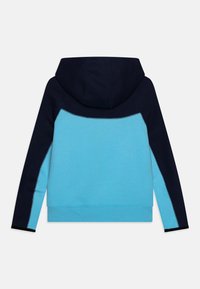 Huppari, jossa on vaalea sininen body ja tummansiniset hihat. Ominaisuuksiin kuuluu sileä rakenne ja kontrastiväriset ompeleet saumoissa.