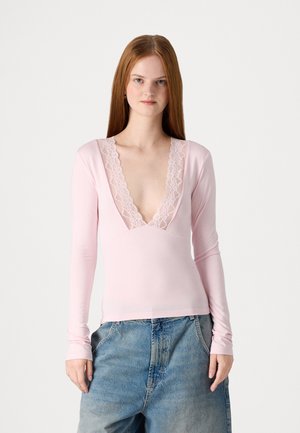 Pink long-sleeve top with a deep v-neck, featuring lace trim along the neckline. Made of a soft, stretchy fabric.