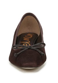 Ballerine in suede marrone con punta arrotondata e un fiocco decorativo realizzato in sottile nastro nero sul davanti. Morbida fodera interna.