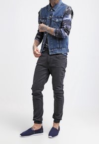 Džínová vesta se zapínáním na knoflíky a dvěma náprsními kapsami, vrstvená přes batikované tričko s dlouhým rukávem. Šedé úzké kalhoty a námořnicky modré pohodlné boty na nazutí.