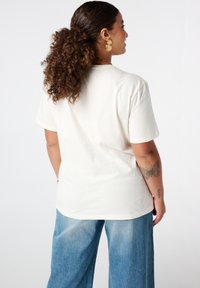 T-shirt en coton couleur crème à manches courtes, coupe décontractée et ourlet arrondi, associé à un jean large bleu clair.