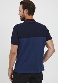 Tengerészkék póló, amely két színű dizájnnal rendelkezik: a felső része sötétebb, míg az alsó része világosabb, piros díszítéssel a karokon.