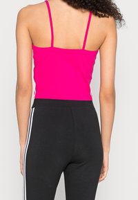 Figureanpassad, klarrosa tanktop med tunna spagetti-remmar, kombinerad med högmidjade svarta byxor med vita sidosträck.