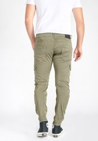 Olijfgroene cargo pants met een slanke pasvorm, voorzien van meerdere achterzakken en een gestructureerde stof, gecombineerd met zwarte high-top sneakers.