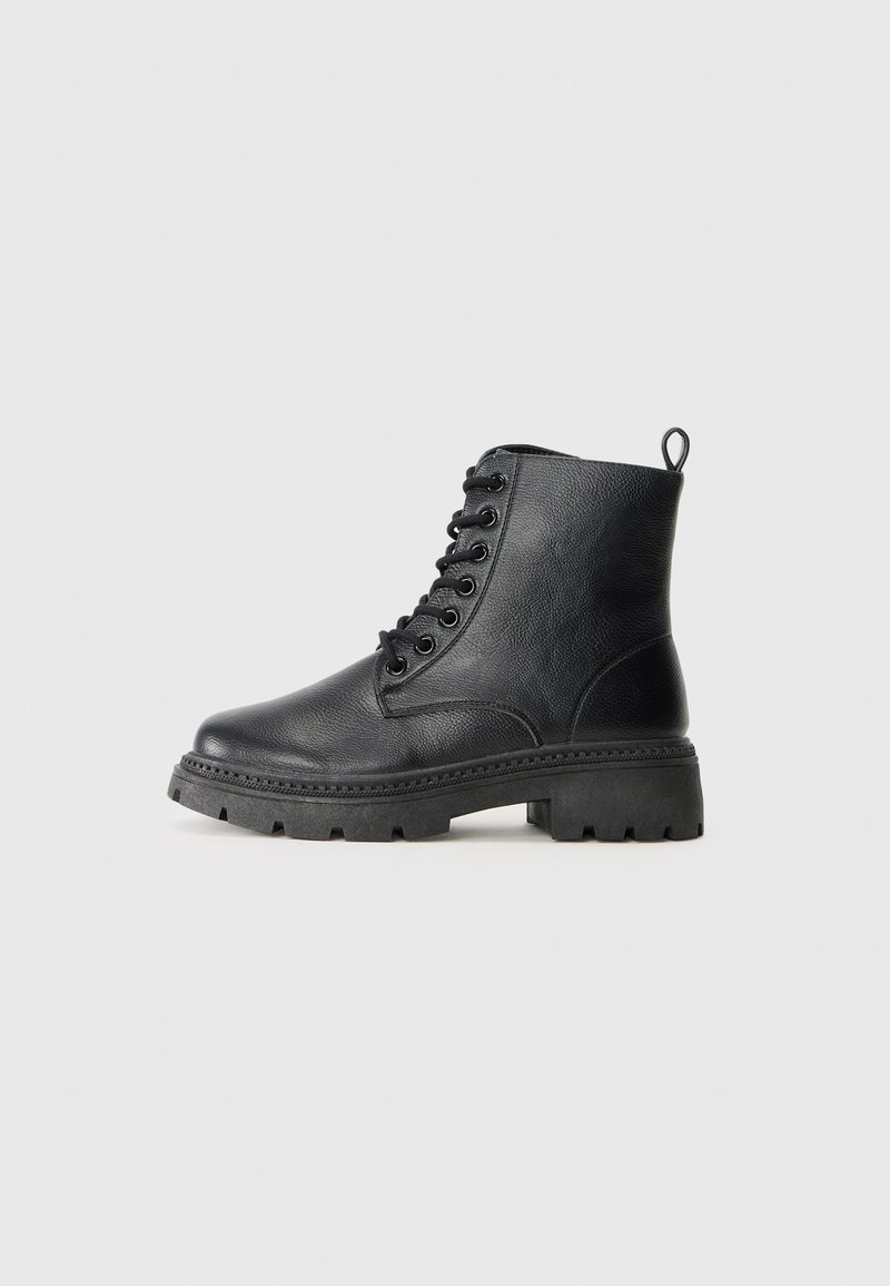 Botte de combat noire en cuir à lacets avec semelle épaisse en caoutchouc et languette à l'arrière, présentée de profil sur un fond gris clair.