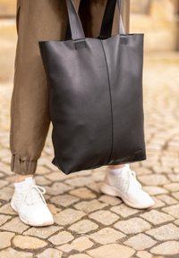 Bolso tote de cuero negro con una textura suave y costuras resistentes. Tiene correas de tela dobles, forma rectangular y detalles de diseño mínimos.