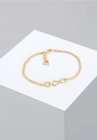 Bracciale color oro con una catena sottile, caratterizzato da un ciondolo a forma di cuore e un simbolo dell'infinito. La chiusura è di tipo semplice a moschettone.