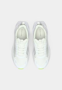 Weiße Sportsneaker mit Mesh-Design, strukturierten Akzenten und flachen Schnürsenkeln. Grüne Details an der Sohle sorgen für einen Farbtupfer.