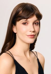 Złoty naszyjnik z zawieszką w kształcie klucza, noszony na czarnej bluzce z cienkimi ramiączkami. Modelka ma długie, ciemne włosy i naturalny makijaż.