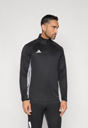 Černá sportovní bunda s límcem na zip, dlouhými rukávy a bílými akcenty Adidas. Má boční pruhy a přiléhavý střih.