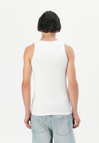 Hvit ribbet tanktopp med rund hals, ermeløs design og tilpasset fasong, parret med lyseblå denimjeans.