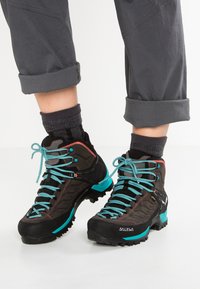Black hiking boots with turquoise laces and accents. Textured fabric upper, sturdy sole with traction, and reinforced ankle support.
