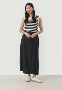 Striped sleeveless top in black and white, paired with a long black skirt. Model wears grey sneakers with white stripes. Simple design.