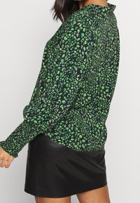 Long-sleeve shirt in black fabric with green and purple floral pattern. Features a collared neck and gathered cuffs. Paired with a leather skirt.