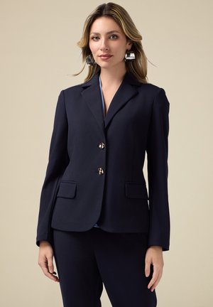 Blazer navy con vestibilità tailored, due tasche frontali e bottoni dorati. Tessuto morbido con rever a punta e maniche lunghe.