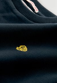 Suéter de punto de cuello redondo en color navy con cuello acanalado y detalle del logo bordado en amarillo. Textura suave y diseño minimalista.