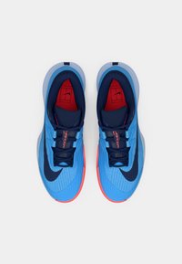 Zilas sporta apavi ar teksturētu augšdaļu, jūras zila akcentiem, sarkanu oderi un rozā zoli. Sānos ir izcila melna swoosh logo.