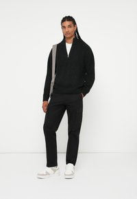 Maglione nero a maglia con design a mezza zip, abbinato a pantaloni cargo neri e sneakers bianche con accenti beigi.