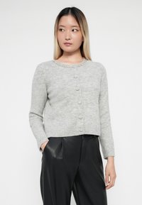 Cardigan en tricot gris avec un col rond, orné d'un ourlet à perles, comportant des fermetures à boutons sur le devant et des manches longues.