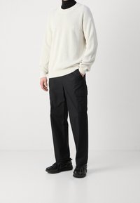 Bílý žebrovaný svetr s kulatým výstřihem, kombinovaný s volně střiženými černými cargo kalhotami se bočními kapsami a černými sportovními botami.