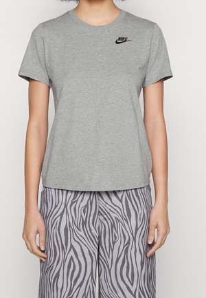 Osoba nosząca jasnoszarą koszulkę Nike z czarnym logo oraz luźne spodnie w czarno-szare paski zebry.