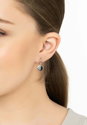 Silver hoop earring featuring a round disc with textured detailing. The earring hangs below the earlobe on a model's ear.