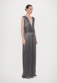 Abito lungo grigio senza maniche con scollatura a V profonda e texture plissettata. La vita è accentuata da una fascia arricciata. Tessuto fluido e morbido.