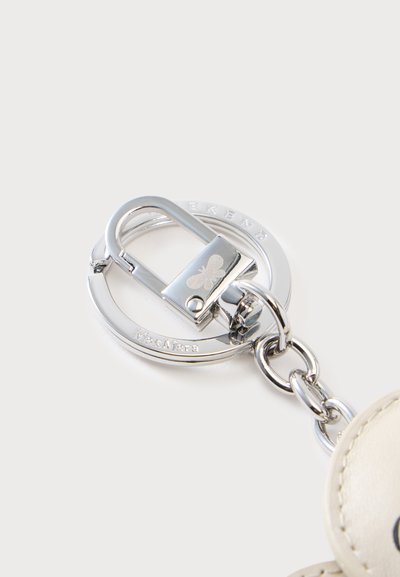 Fermoir de porte-clés en argent attaché à un anneau en métal gravé de "Max Mara" à côté d’un cuir crème avec coutures.