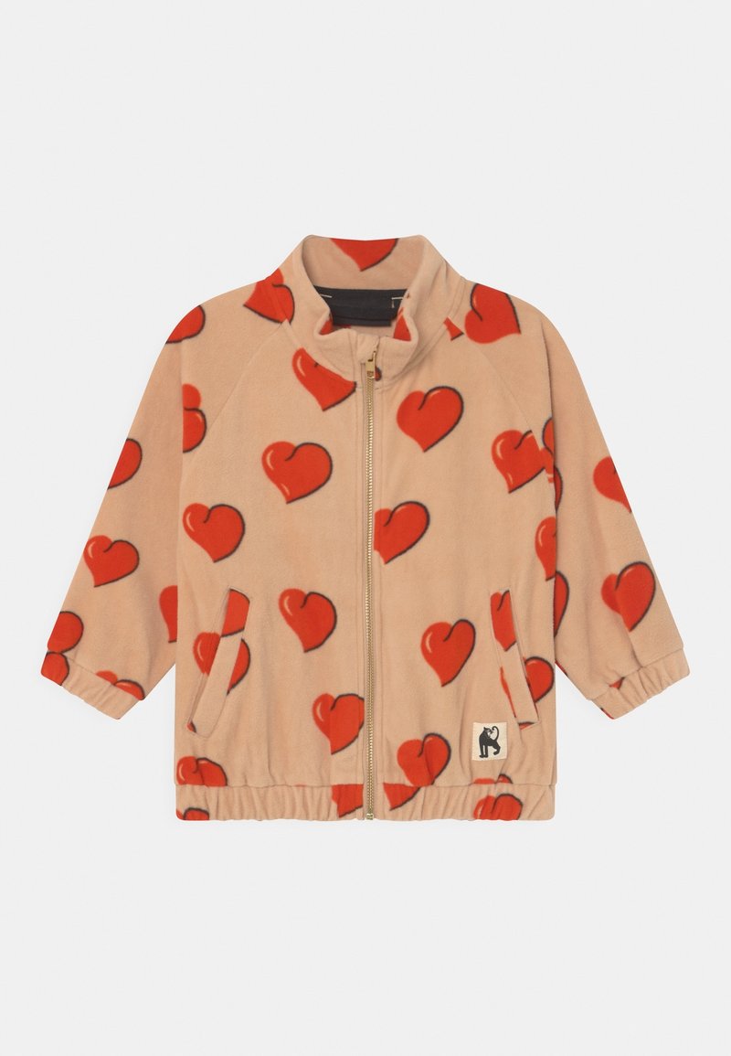 Veste beige zippée avec motifs de cœurs rouges, poignets et ourlet élastiques, poches avant et un petit patch logo chat noir en bas à gauche.