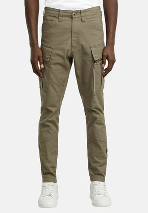 Pantalons cargo en tissu coton léger couleur kaki clair ; dotés de plusieurs poches, de détails zippés, d'une coupe fuselée et de coutures renforcées. Associés à des baskets blanches.