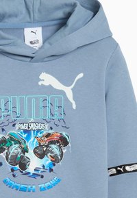 Felpa blu con logo Puma, testo "Power Smashers" e grafica di due monster truck che si scontrano con fulmini e "Crash Zone" sotto.