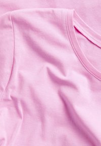 Lichtroze katoenen T-shirts met een gladde textuur. Heeft een ronde halslijn en korte mouwen. De stof vertoont zachte plooien.