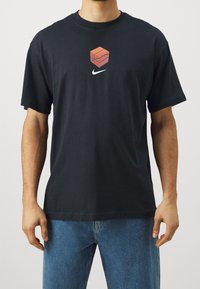 Camiseta de algodón negra con un gráfico de un cubo rosa apilado y el logo blanco de Nike en el pecho. Mangas cortas y corte relajado.