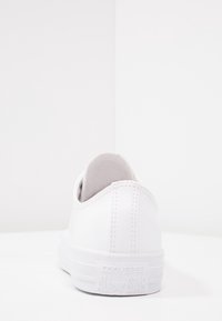 White canvas sneaker with a low-top design, textured material, stitching details, and a rubber sole featuring a logo on the heel.