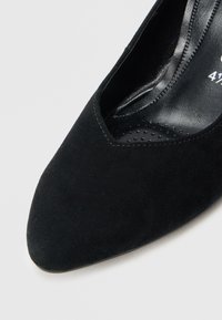 Černý semišový vysoký podpatek s špičatou špičkou a výřezovým designem. Vnitřek je vybaven hladkou černou podšívkou s perforacemi pro lepší prodyšnost.