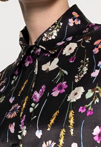 Black shirt featuring a floral pattern in various colors. Made of smooth fabric with a collared neckline and button-up front.