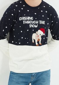 Marineblau- und cremefarbener gestrickter Pullover mit einem festlichen Hundedesign, der einen Weihnachtsmannhut trägt, und dem Text "Durch den Schnee flitzen", strukturiertes Muster.