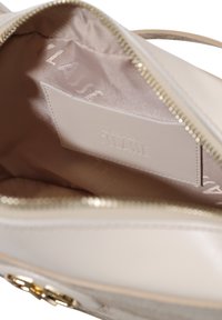 Interno di una borsa a mano in pelle beige con una fodera setosa, zip dorata e etichetta con logo in rilievo. Texture liscia senza motivi visibili.