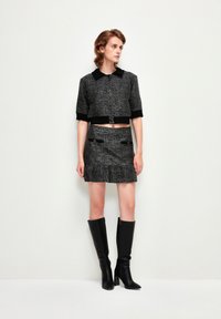 Zwart-grijze tweed cropped jas met een kraag, gecombineerd met een bijpassende rok met een gerimpelde zoom en zwarte accenten; gedragen met hoge zwarte laarzen.