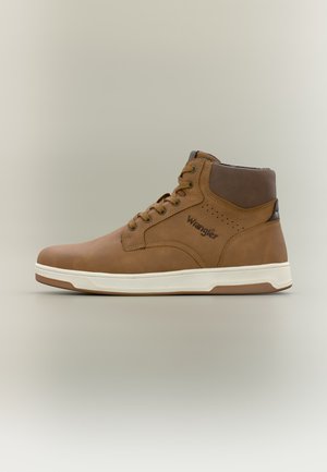 Chaussure décontractée montante marron avec semelle blanche et lacets, col rembourré à la cheville, et logo "Wrangler" sur le côté.