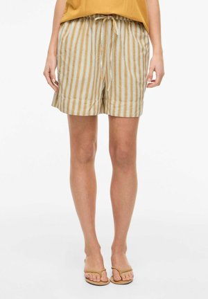 Kvinne iført beige og hvite vertikalt stripete shorts med elastisk midje og snor, kombinert med brune flip-flop sandaler.