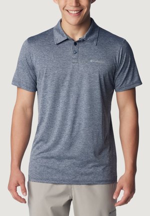 Mężczyzna ubrany w niebieskoszary polo z krótkim rękawem, kołnierzykiem i dwoma guzikami, w połączeniu z jasnoszarymi spodniami.