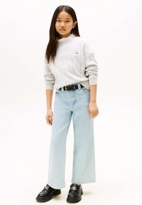 Grauer gestrickter Pullover mit Zopfmuster, hellblaue Jeans mit weitem Bein und schwarze Loafer mit goldener Schnallendetail.