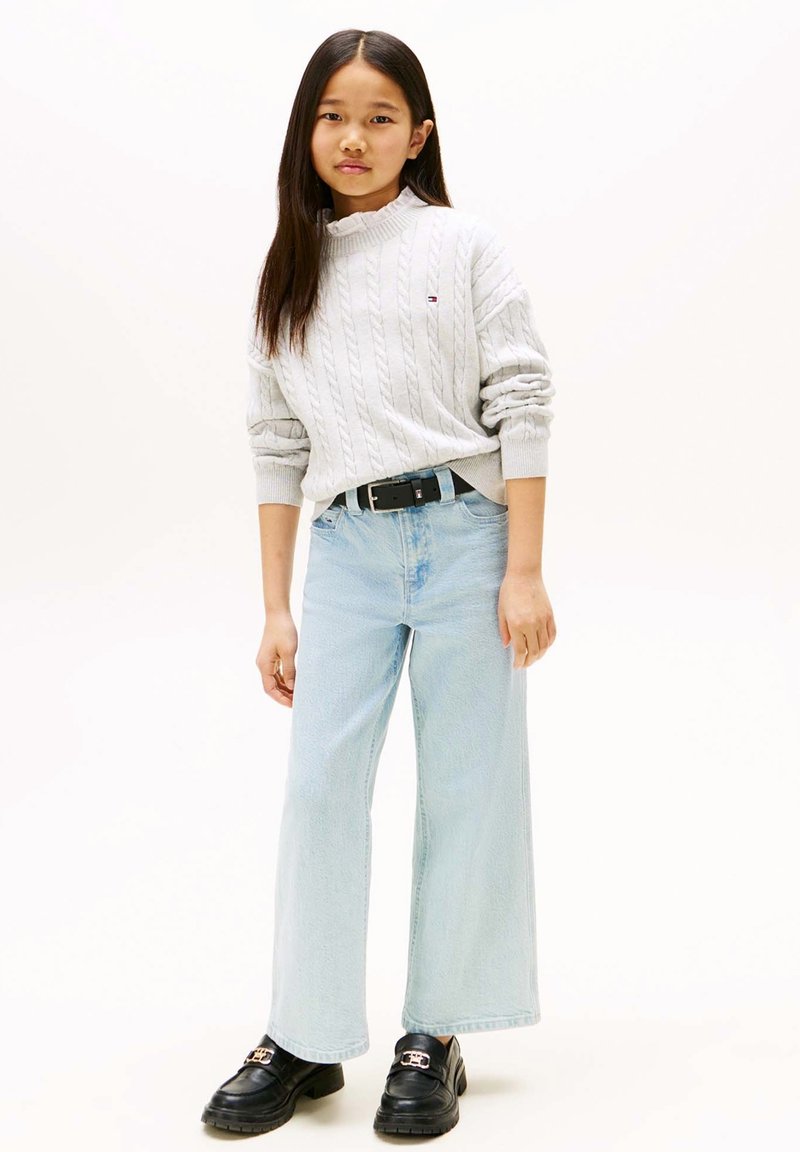 Grauer gestrickter Pullover mit Zopfmuster, hellblaue Jeans mit weitem Bein und schwarze Loafer mit goldener Schnallendetail.