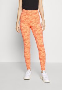 Oranga leggings med blommönster, med hög midja och en åtsittande passform. Kombinerat med vita sneakers och en svart topp.