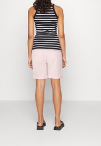 Camiseta sin mangas de rayas blancas y negras, combinada con pantalones cortos rosa claro, con dobladillos doblados. Se lleva con sandalias de plataforma negras.