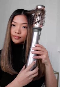 Strumento per lo styling dei capelli con un corpo metallico cilindrico, dettagli in rosa dorato e una testa a spazzola con setole. Presenta un'impugnatura testurizzata per una migliore maneggevolezza.