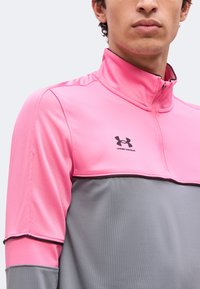 Άνδρας που φοράει αθλητικό μπλουζάκι Under Armour με φερμουάρ, διχρωμίας ροζ και γκρι, με ψηλό γιακά, εμφανίζοντας τον άνω κορμό και μέρος του προσώπου.